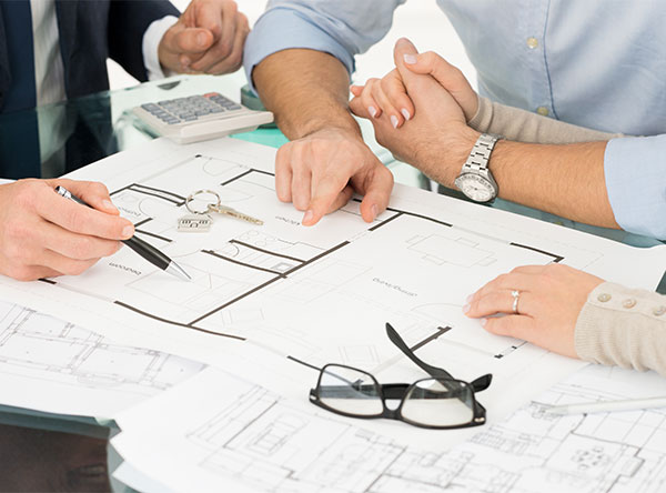 couple holding hands and looking a home blueprints with agent